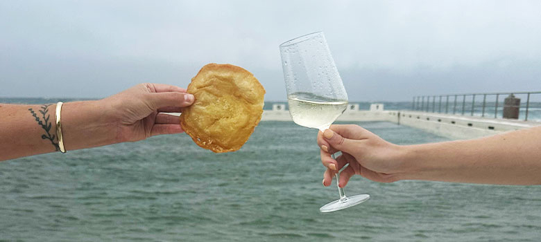 A potato scallop and a glass of wine with the beach in the background