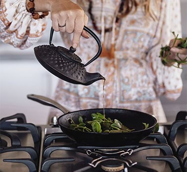 Mindy Woods pouring liquid onto leaves over a stovetop