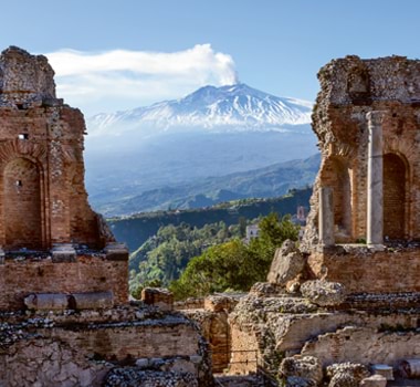 Mount Etna stirs in the background of the ancient Teatro Greco in Taormina, Sicily