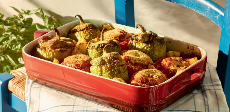 A red oven dish on a rustic chair filled with chef Carolina Doriti's stuffed tomatoes and peppers with potato
