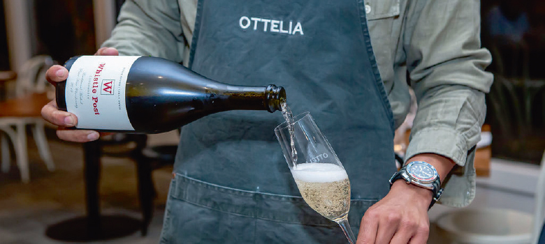 A glass of sparkling wine being poured by someone wearing an Ottelia apron